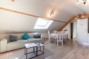 Une pièce de style loft avec un plafond en pente, une lucarne, un canapé, une table à manger avec des chaises et un réfrigérateur blanc.