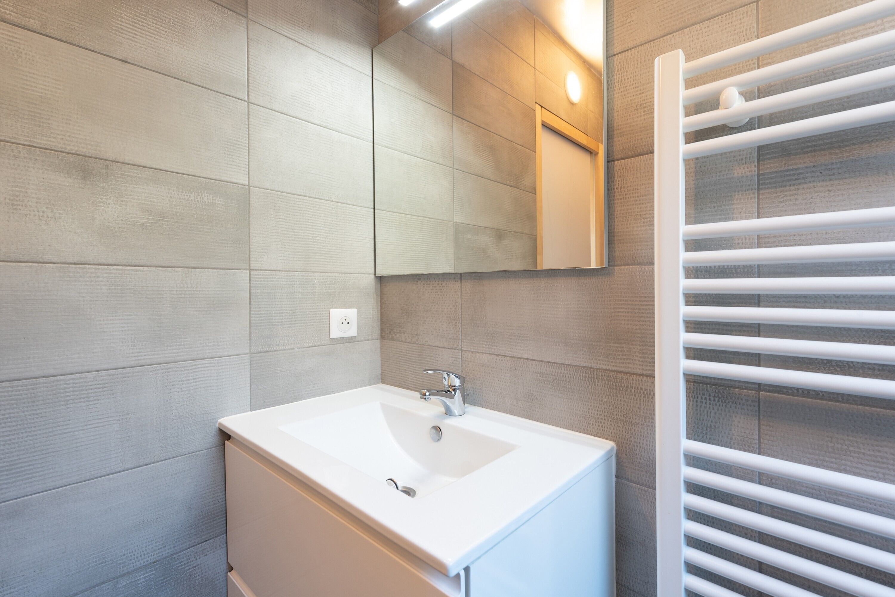 Une salle de bain avec un lavabo blanc, un miroir et un porte-serviettes.