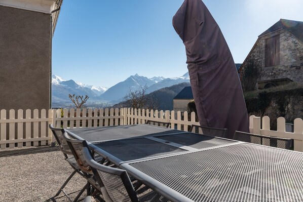 A metal table with a mesh top, a white picket fence, and a mountainous landscape in the background.