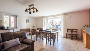 A spacious living area with a leather sofa, dining table, and chairs, a wooden cabinet, and a large window with a view. - Gîte d'Ayzi – Charming Rental with Panoramic Views, Ideal for Families or Friends, 15 Minutes from Lourdes (Ouzous)