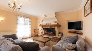 Een woonkamer met een open haard, bank, televisie en een kroonluchter.