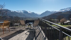 Een houten terras met buitenmeubilair, met uitzicht op besneeuwde bergen.