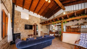 Una sala de estar acogedora con pared de piedra, chimenea, sofá azul y techo de madera.