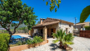 Una casa de piedra con piscina, rodeada de vegetación y un cielo azul despejado.