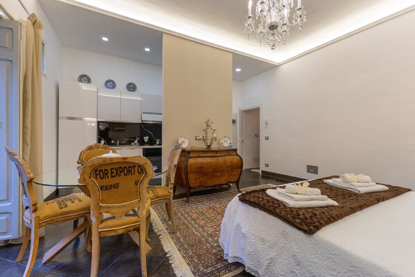 A hotel room with a bed, a chair, a dresser, a mirror, and a chandelier.
