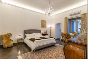 Une chambre à coucher avec un grand lit, un lustre, une petite table avec une lampe, une chaise et une commode.