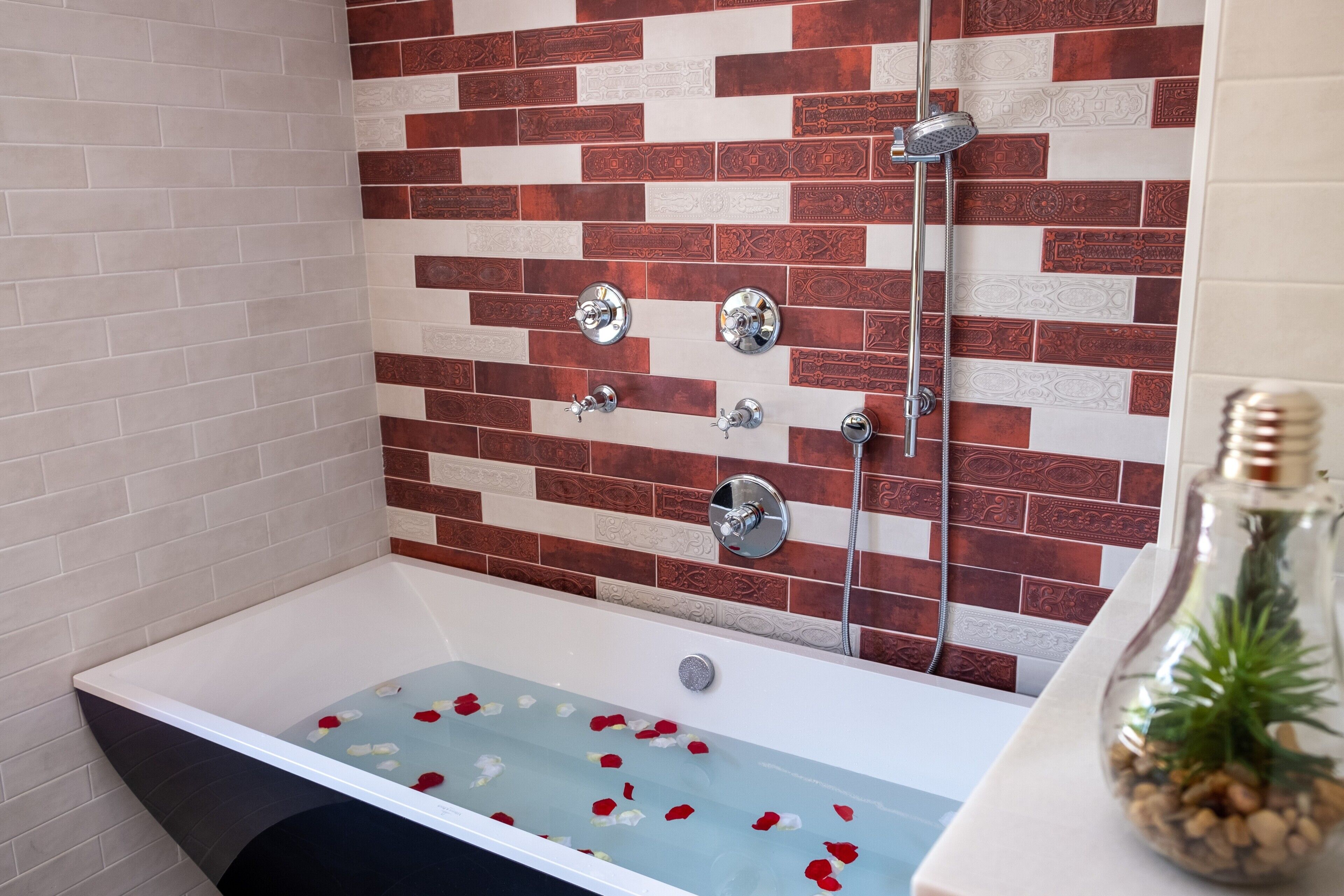 Una vasca da bagno con petali di rosa, un soffione e un vaso di vetro con pigne.