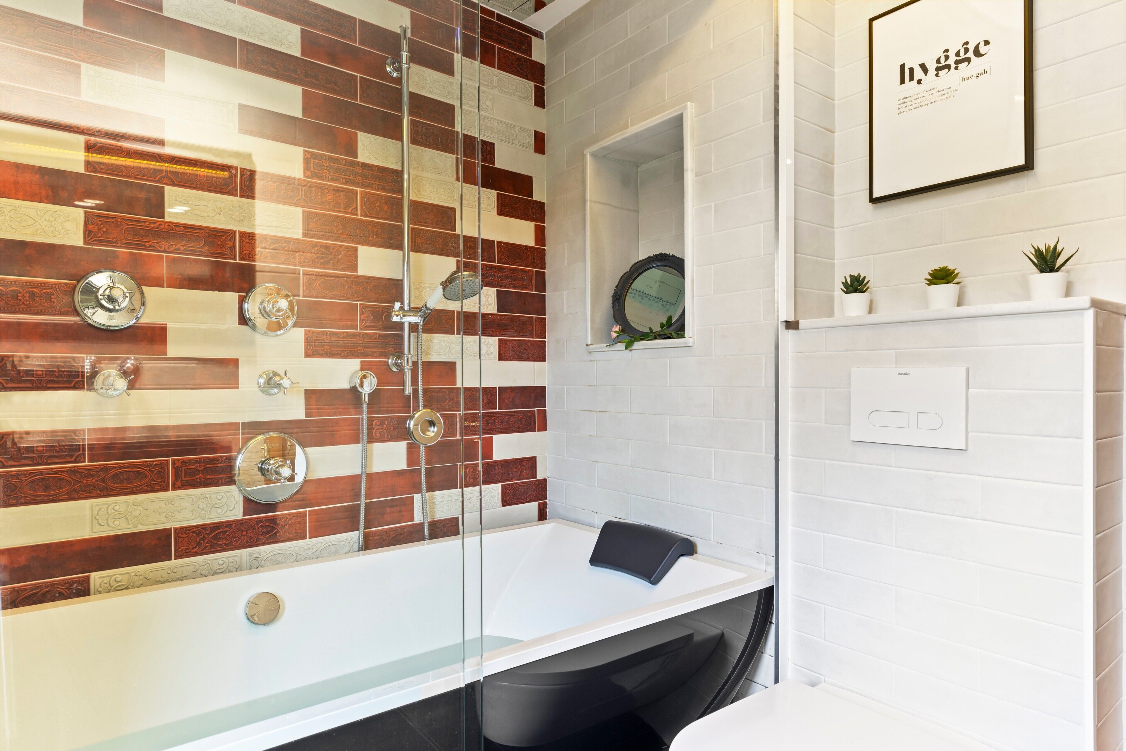 Ein modernes Badezimmer mit einer gläsernen Duschkabine, einer weißen Badewanne und einer weißen Fliesenwand mit dekorativem Muster.