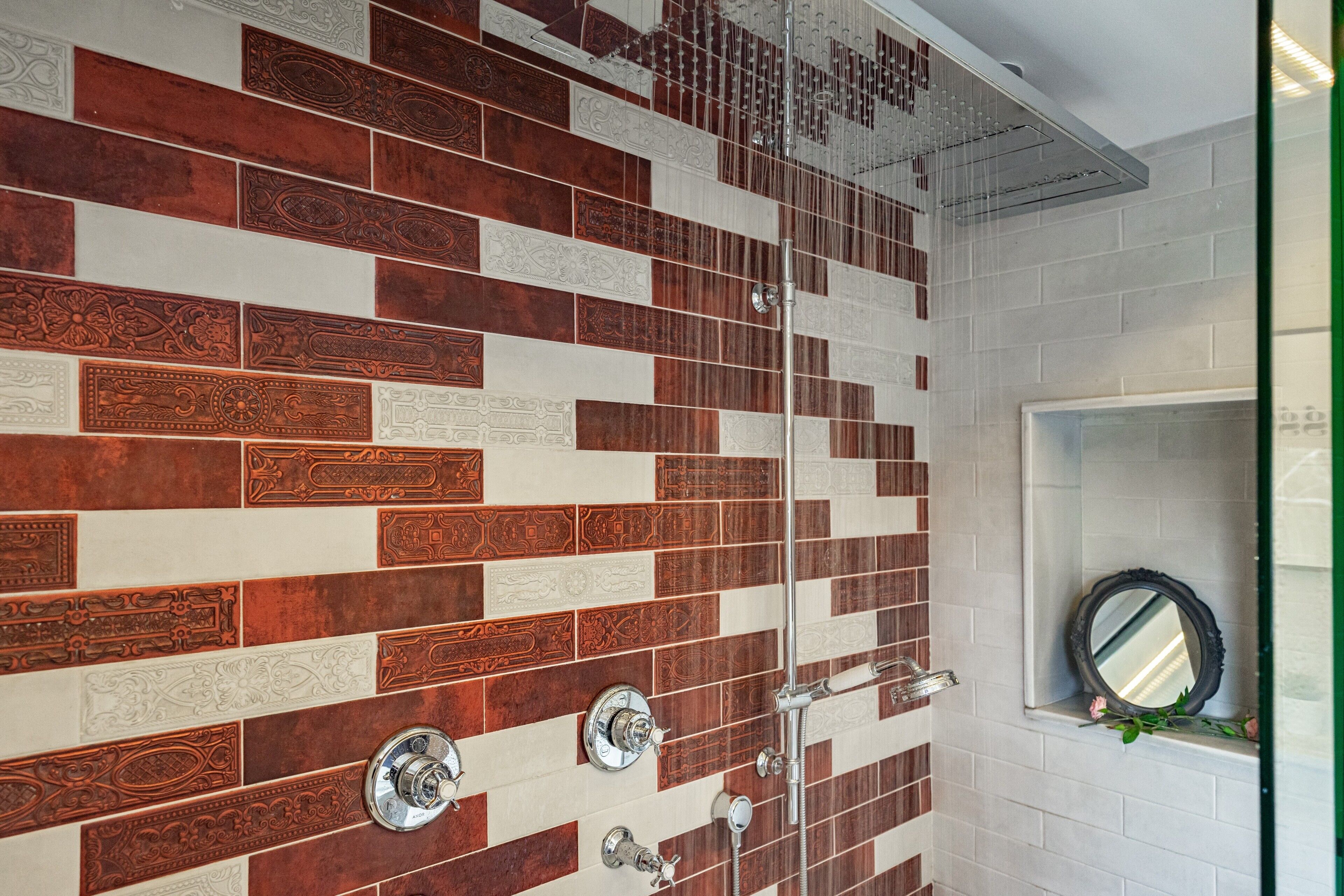A bathroom with a patterned tile wall, a shower area, and a mirror with a rose decoration.