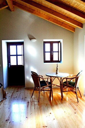 Ein Zimmer mit Holzboden, einem Esstisch mit Stühlen, zwei Fenstern und einer Decke mit freiliegenden Balken.
