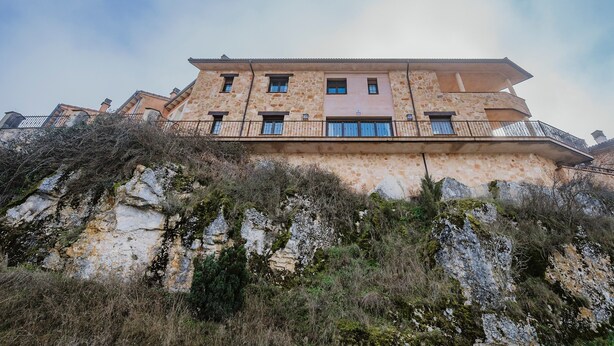 A multi-story building with balconies, situated on a rocky hillside.