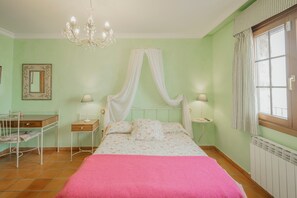 Quarto com cama, mesas de cabeceira, espelho, lustre e janela com cortinas.