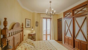 A bedroom with a wooden bed, a nightstand, a chandelier, and a large window with curtains.