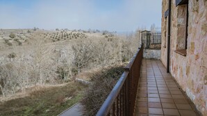 A balcony with a view of a rural landscape, a stone wall, and a metal railing.