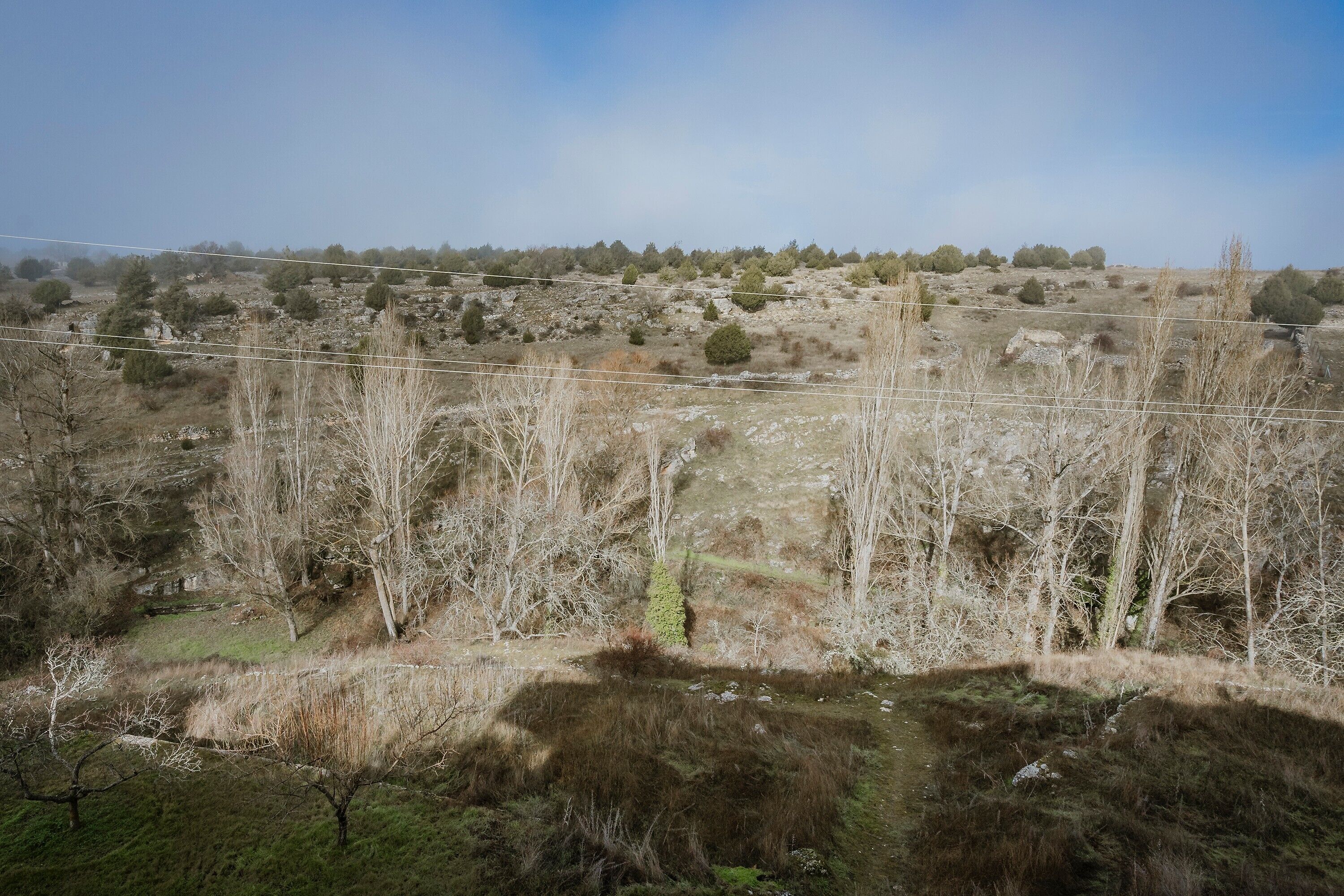 Paisaje rural con vegetación escasa, un pequeño cuerpo de agua y cielo despejado.