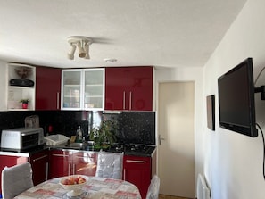 A kitchen with red cabinets, a microwave, a stove, and a dining table with a bowl of fruit.