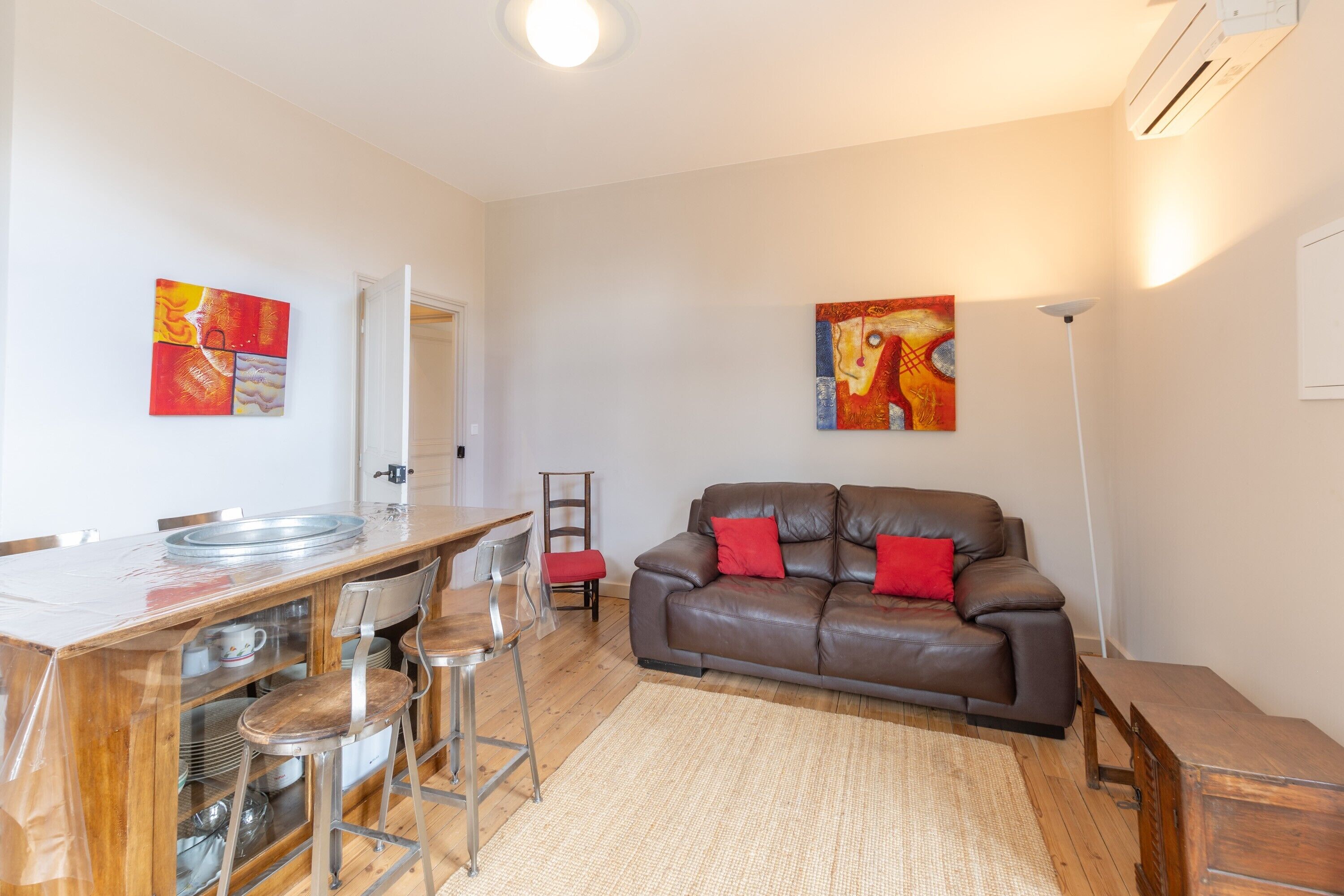 A living room with a brown leather sofa, a dining table with metal chairs, and two abstract paintings on the walls.