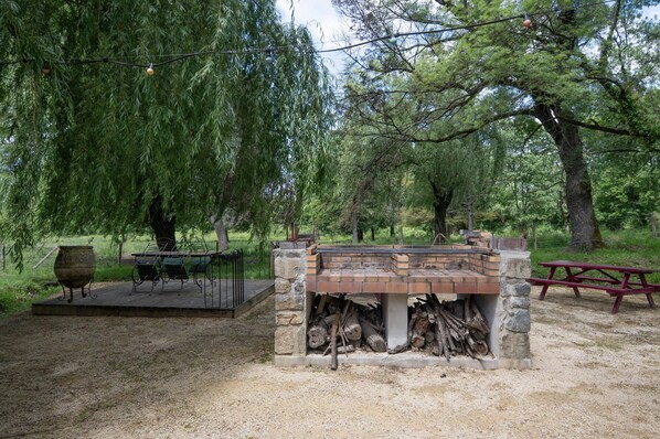 A rustic outdoor seating area with a brick fireplace, a metal table, and a picnic table.