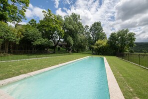Une piscine rectangulaire entourée d’une pelouse et délimitée par une clôture en métal noir.