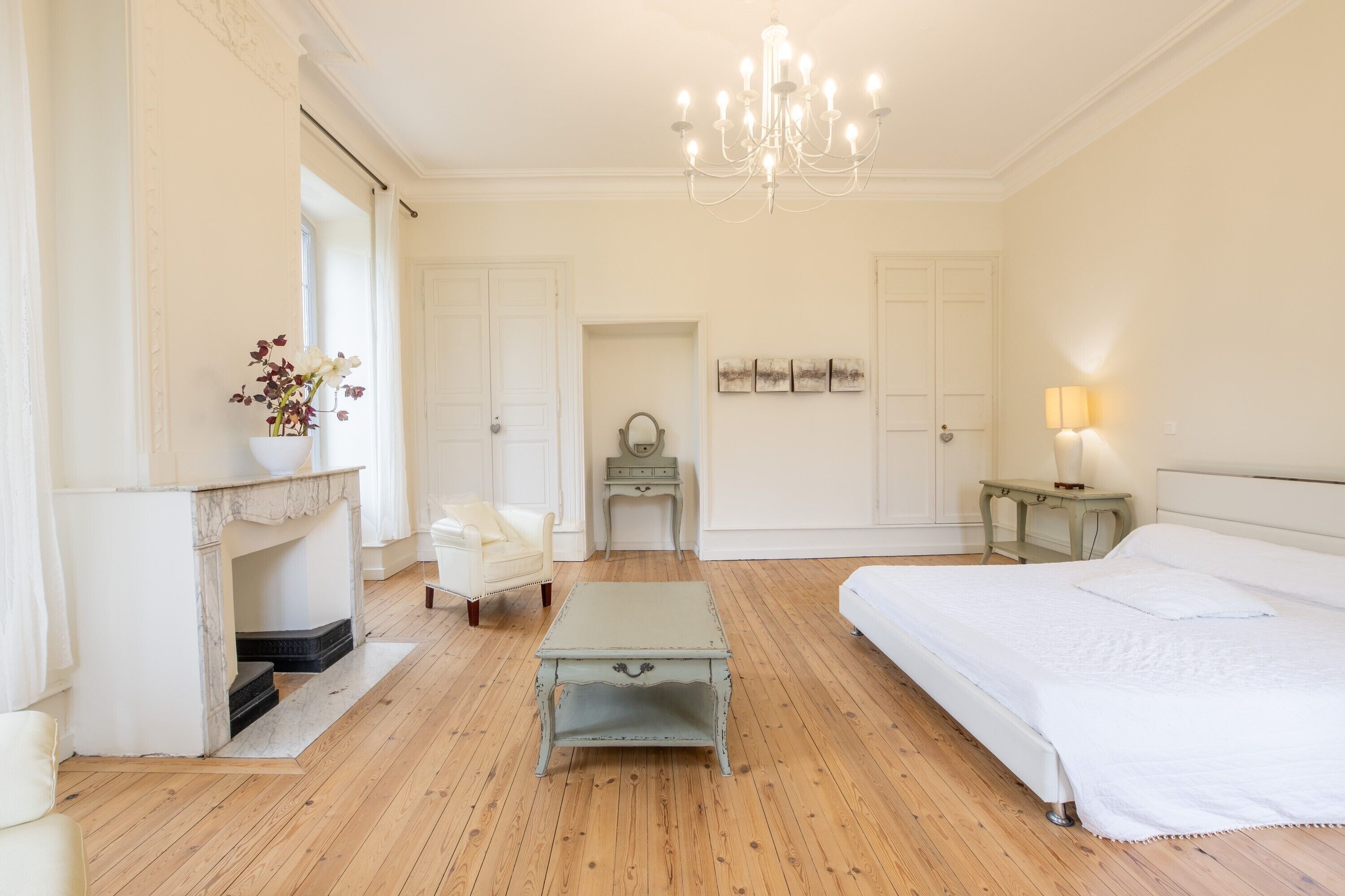 Een slaapkamer met een bed, een kaptafel, een dressoir, een stoel, een klein tafeltje en een kroonluchter.