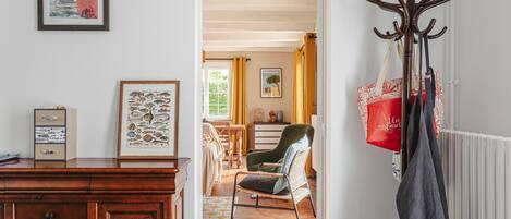 A room with a wooden dresser, a framed picture, a chair, and a coat rack with bags.