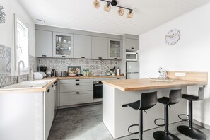A modern kitchen with grey cabinets, a wooden countertop, and three black bar stools. -  Charming House with Terrace, Parking, and Comfort 10 min from Beach and Harbor (Saint-Trojan-les-Bains)