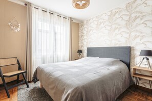 Une chambre à coucher comprenant un lit, une chaise, une table de chevet, une lampe et un mur orné d’un motif de feuilles.