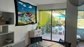 Une pièce avec une grande fenêtre, un tableau, une table avec des chaises et un petit meuble.