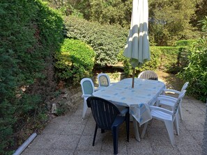 An outdoor patio with a table and chairs, surrounded by greenery.