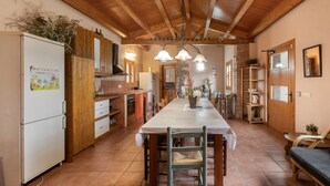 A kitchen with wooden beams, a dining table, chairs, a refrigerator, and a potted plant.