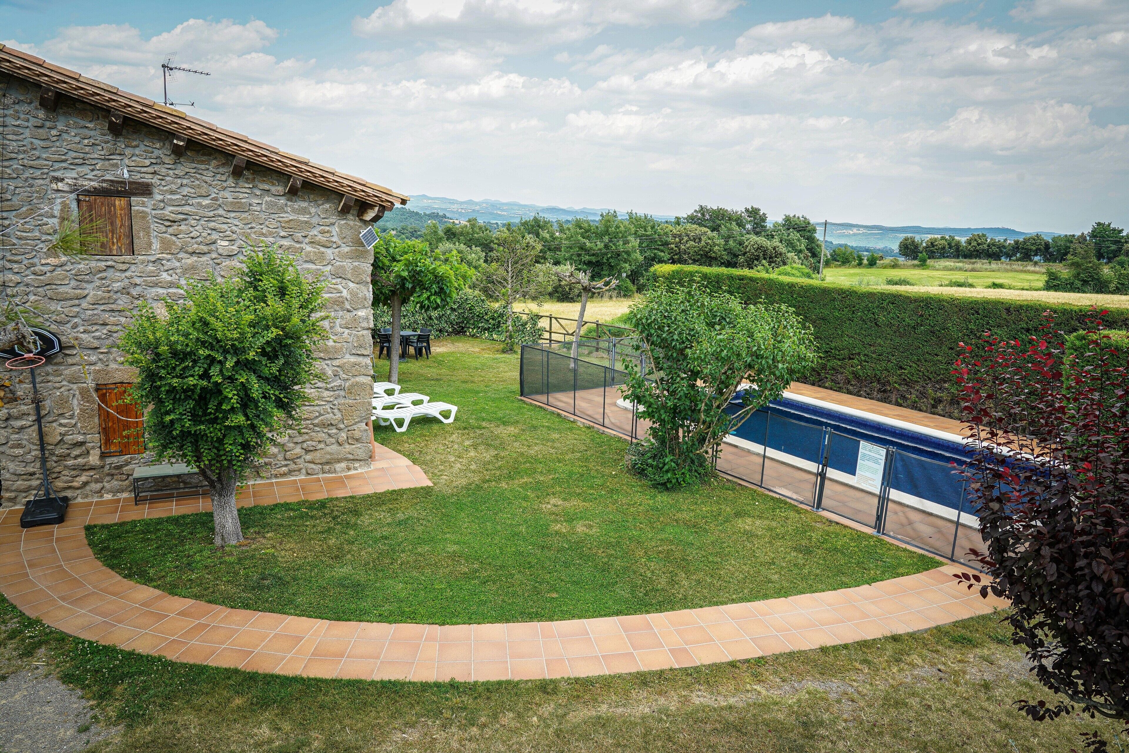 A stone house with a swimming pool, surrounded by a well-maintained lawn and a view of the countryside.