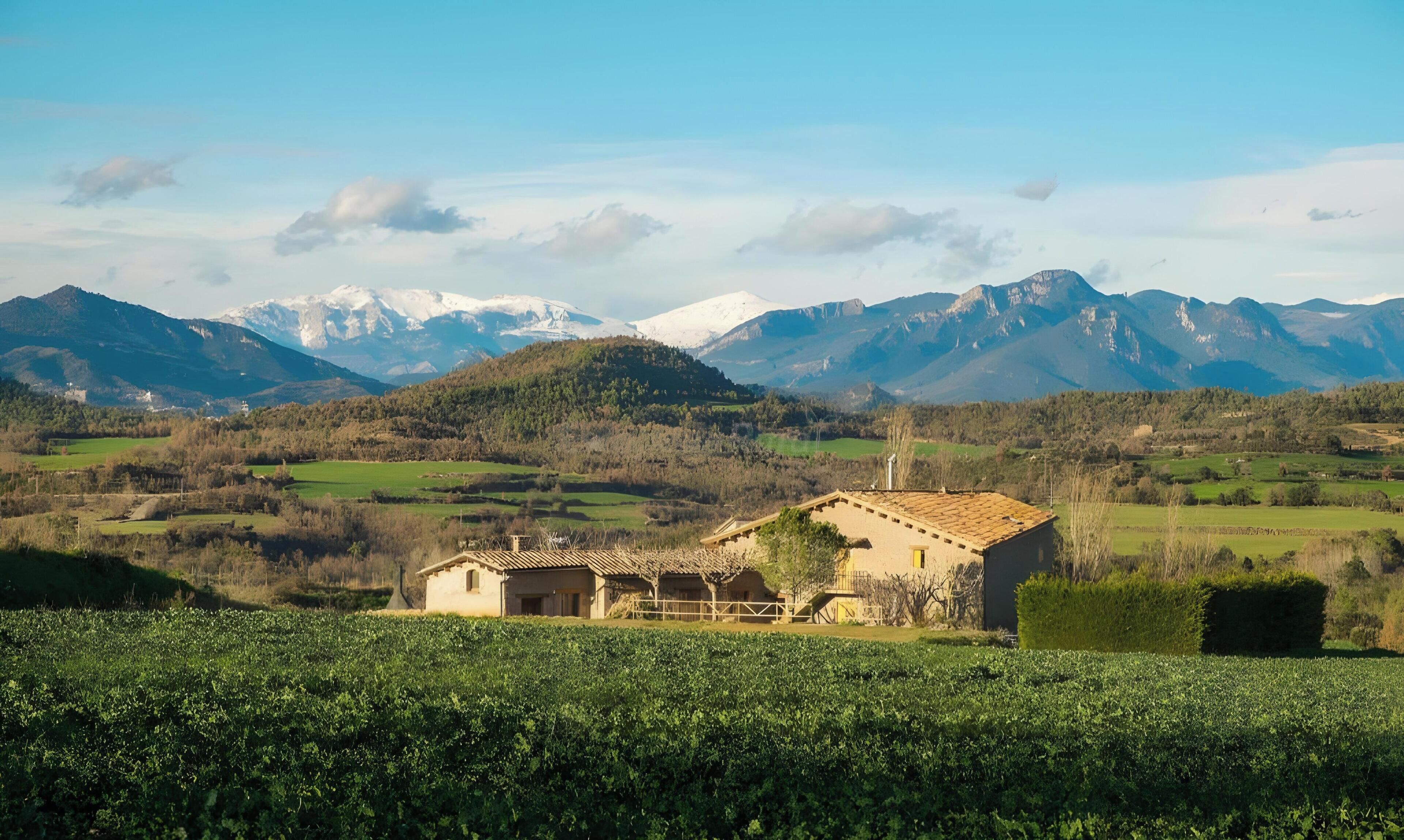 A rural house with a tiled roof, surrounded by fields and mountains.