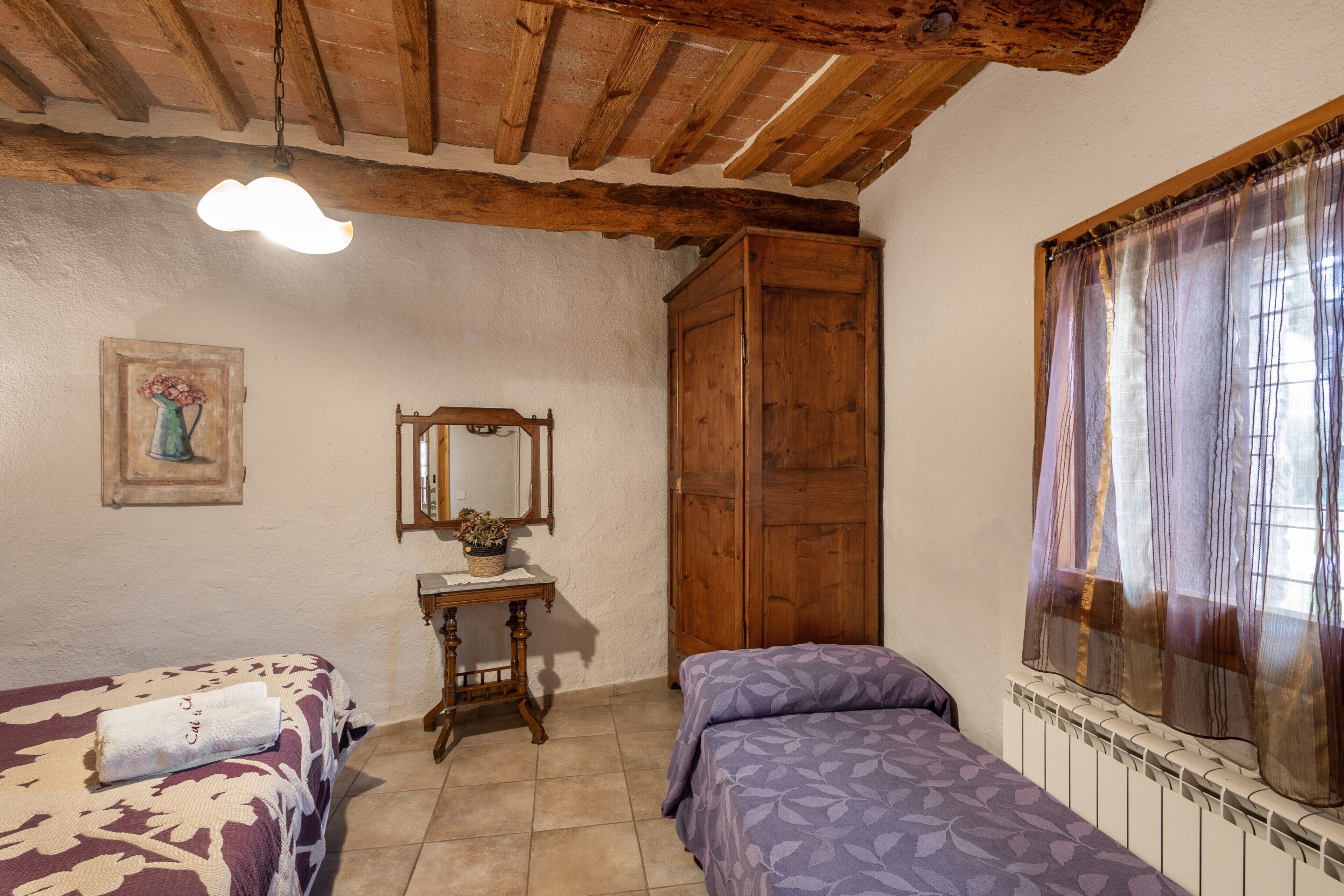 A room with two beds, a wooden wardrobe, a small table with a mirror, and a window with curtains.