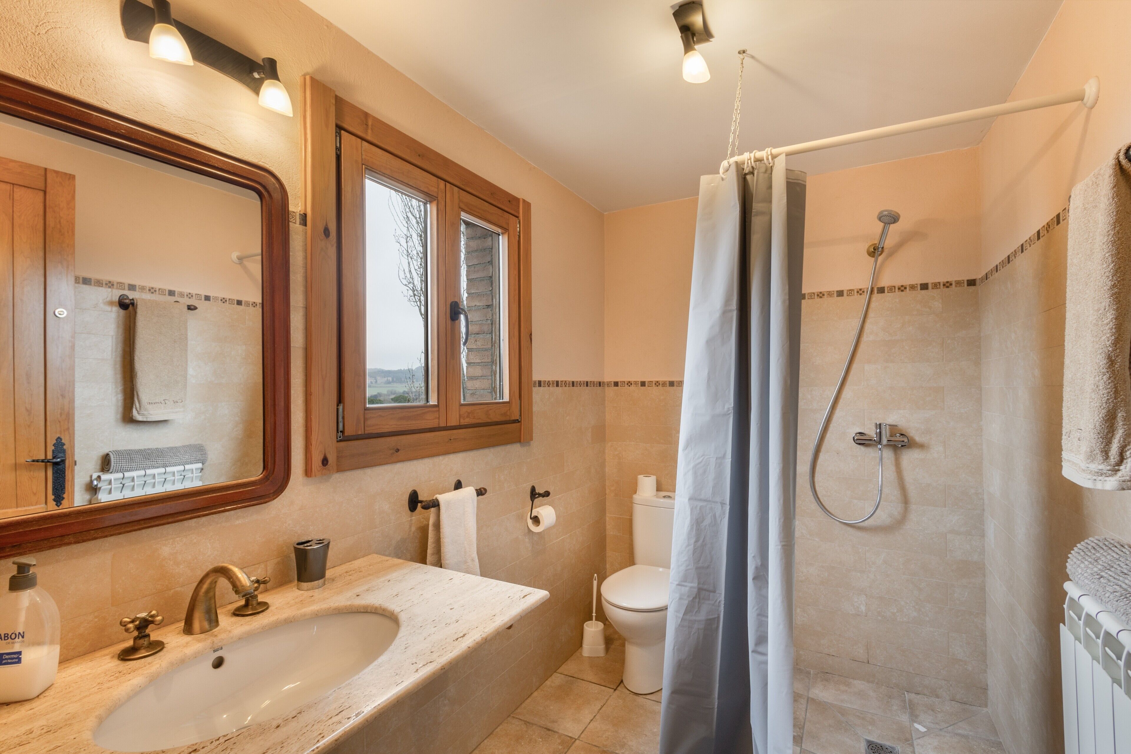 A bathroom with a sink, mirror, toilet, shower, and a window.