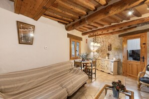 A cozy living room with a sofa, a dining table with chairs, a kitchen area, and wooden beams on the ceiling. - Country House 'Cal Torrentí' with Mountain View, Private Pool and Wi-Fi (Casserres)