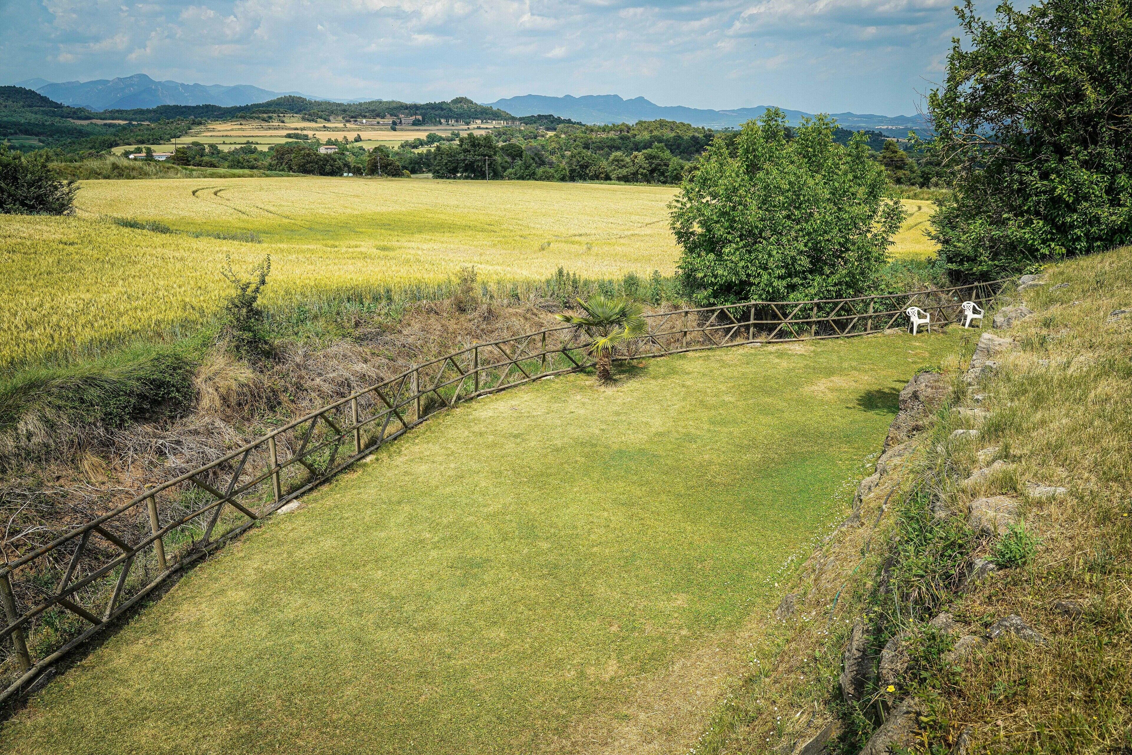 A rural landscape with a fenced area, a tree, and a distant view of mountains.