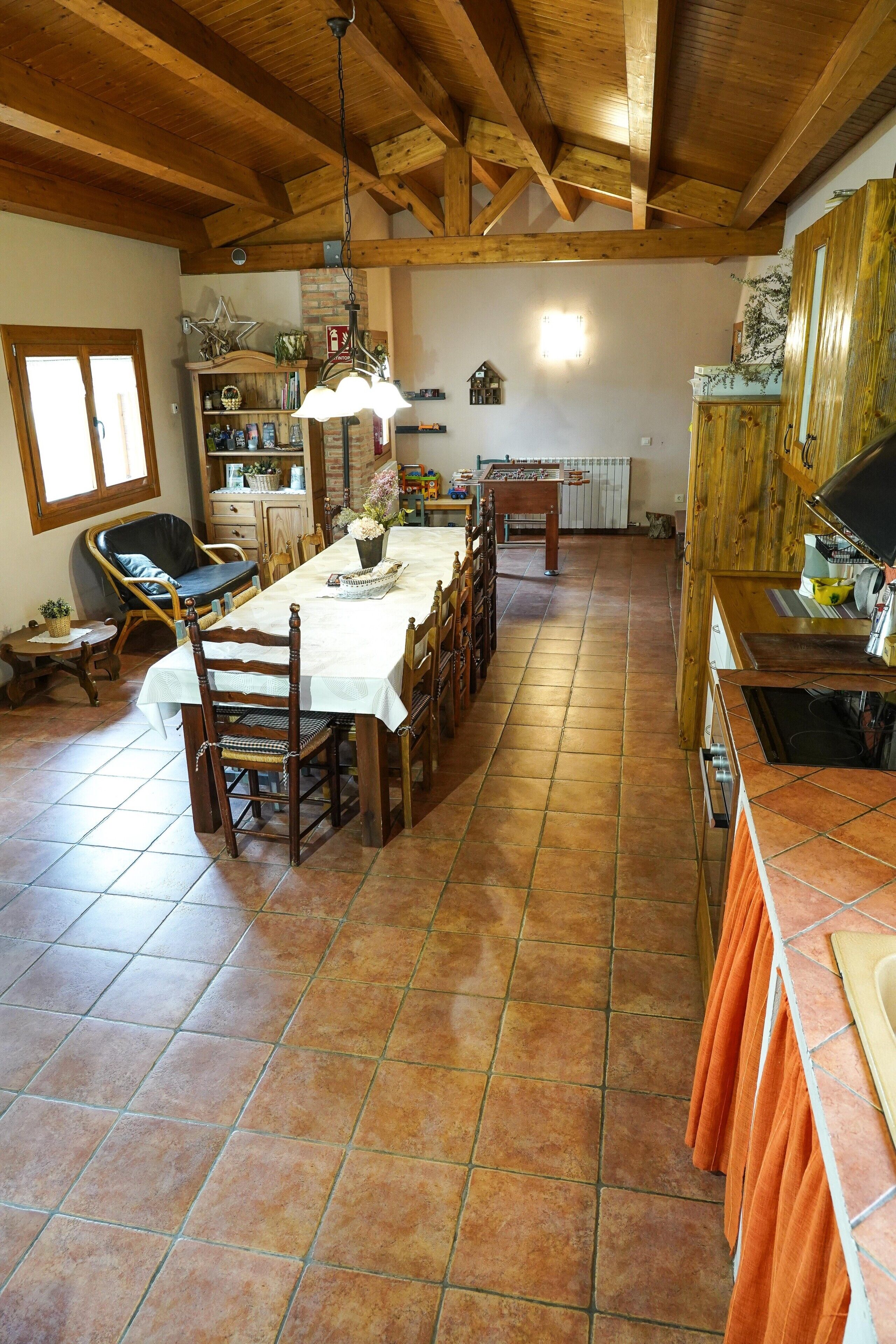 Una cocina rústica con una mesa de madera larga, sillas y un colgador de luz.