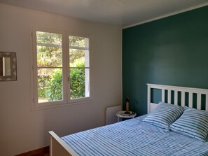 A bedroom with a bed, a window, a bedside table, and a wall-mounted mirror.
