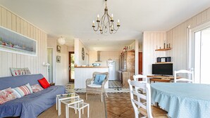 Un salon chaleureux avec un canapé, une table à manger, une cuisine en arrière-plan et un lustre.