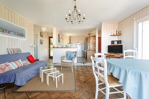 Un salon chaleureux avec un canapé, une table à manger, une cuisine en arrière-plan et un lustre.