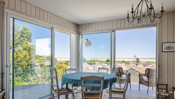 Un espace repas avec une table ronde, des chaises et une vue dégagée grâce à de grandes fenêtres.