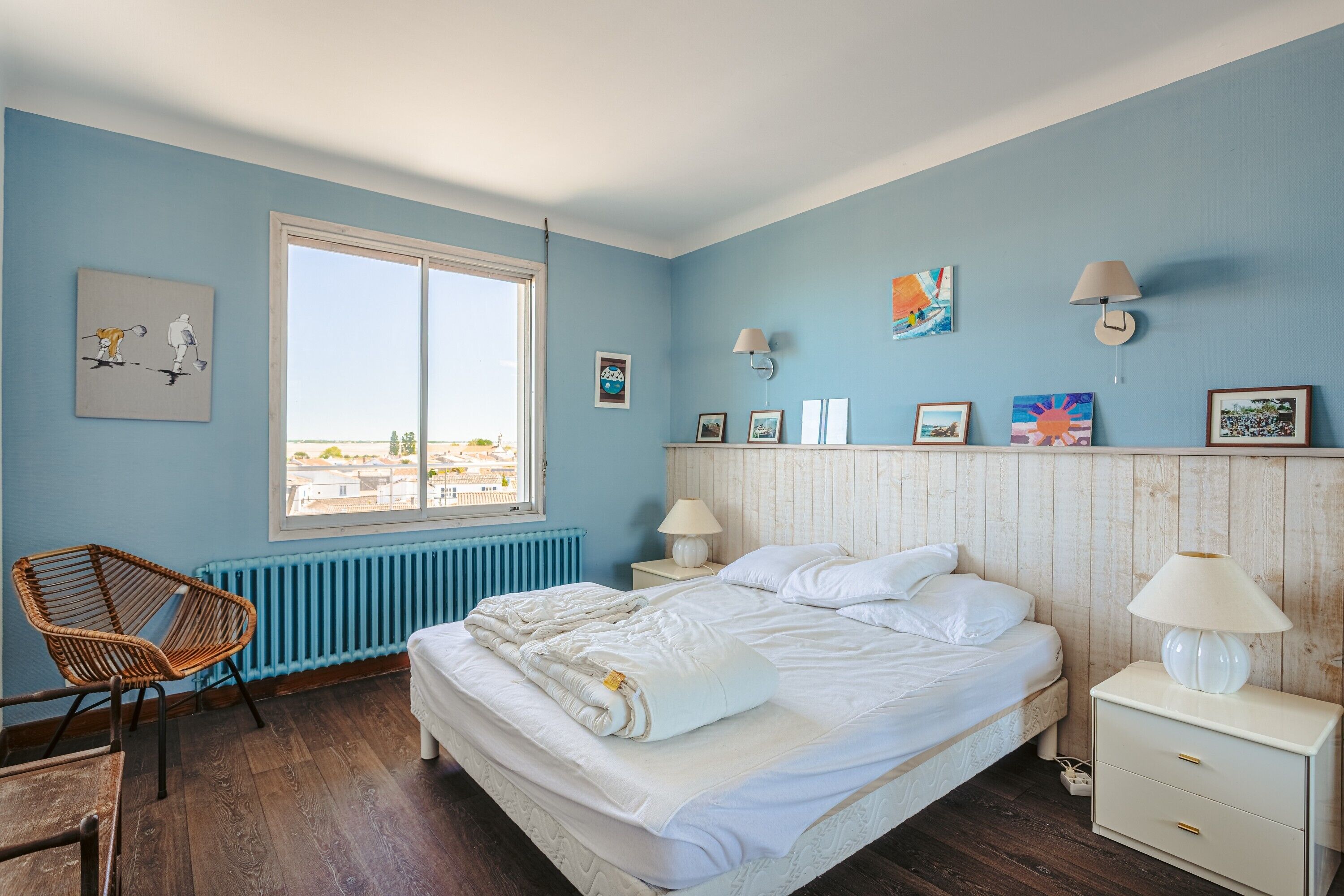 Un dormitorio con cama, una silla, una mesita de noche, una lámpara y una ventana.
