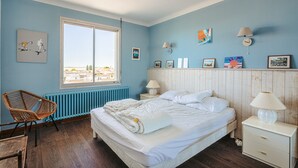 Une chambre à coucher avec un lit, une chaise, une table de chevet, une lampe et une fenêtre.