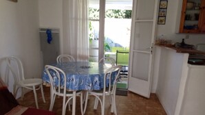 A dining area with a table and chairs, a kitchen area with cabinets, and a view of greenery outside. - Tranquil Escape: House with Private Garden, 150m from the Forest and 20min to the Beach (Saint-Trojan-les-Bains)