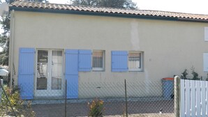 A two-story building with a beige exterior, blue shutters on the windows, and a white fence in front. - Tranquil Escape: House with Private Garden, 150m from the Forest and 20min to the Beach (Saint-Trojan-les-Bains)