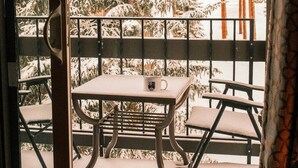 Ein Balkon mit Tisch und Stühlen mit Blick auf einen verschneiten Wald.