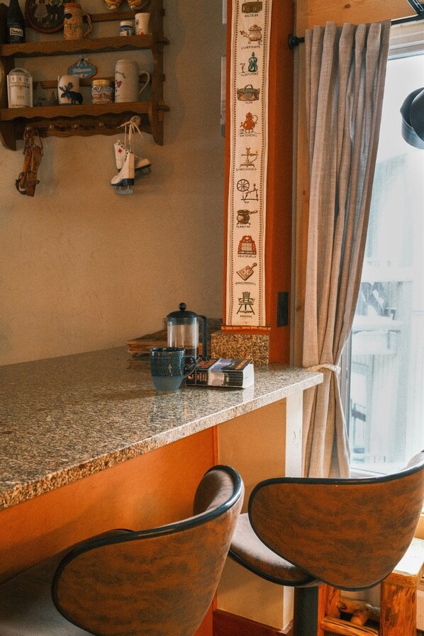A kitchen with a granite countertop, a coffee maker, and a decorative wall hanging. There are two chairs in front of the counter.