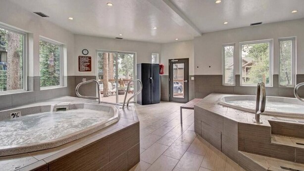 Ein Wellnessbereich mit zwei Whirlpools, einer Holzbank und einer Tür, die nach draußen führt.