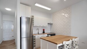 A modern kitchen with white cabinets, a stainless steel refrigerator, a wooden dining table, and white chairs.