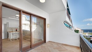 A balcony with a view of the sea, a sliding glass door leading to a kitchen, and a herringbone-patterned floor.
